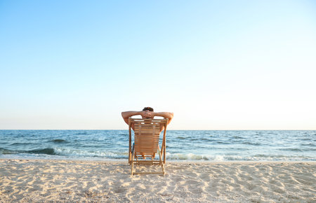 Young man relaxing in deck chair on beach near seaの写真素材