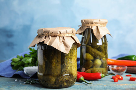 Jars with pickled cucumbers on wooden table against blue backgroundの写真素材