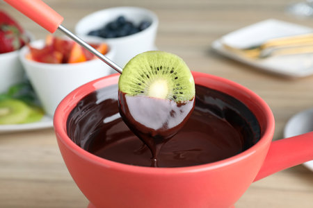 Dipping kiwi slice into pot with chocolate fondue on table, closeupの写真素材