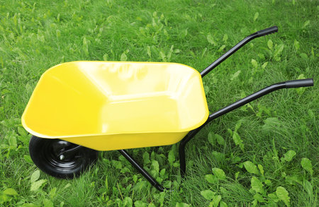 Yellow wheelbarrow on green grass outdoors. Gardening toolの写真素材