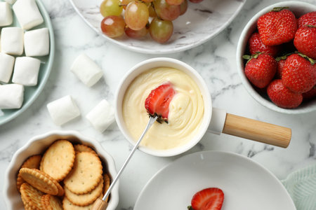 Dipping strawberry into fondue pot with white chocolate on marble table, top viewの写真素材