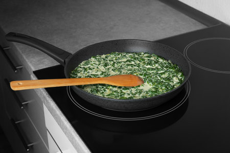 Tasty spinach dip with wooden spoon in frying pan on kitchen stoveの写真素材