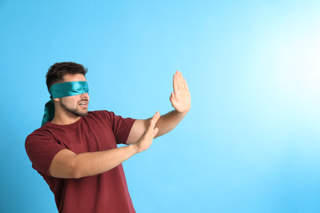 Young man with blindfold on blue background, space for textの写真素材