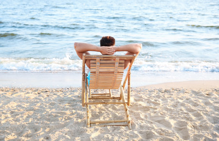 Young man relaxing in deck chair on beach near seaの写真素材