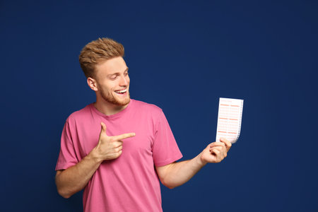 Portrait of happy young man with lottery ticket on blue backgroundの写真素材