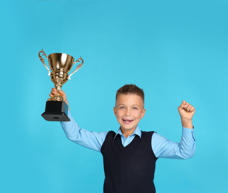 Happy boy in school uniform with golden winning cup on blue backgroundの写真素材