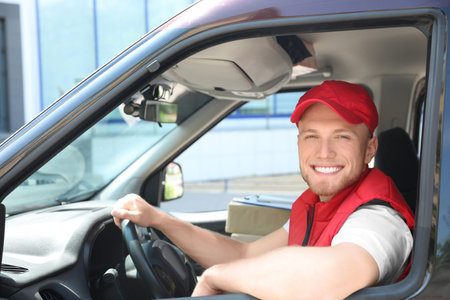 Young courier with parcels in delivery car