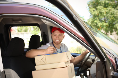 Young courier with parcels and clipboard in delivery carの写真素材