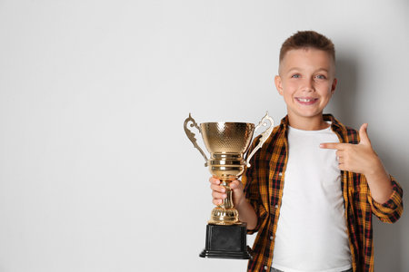 Happy boy with golden winning cup on light background. Space for textの写真素材