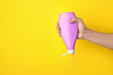 Woman pouring cosmetic product from bottle on yellow background, closeup. Space for textの写真素材