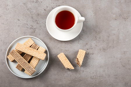 Plate of delicious wafers with cup of tea on grey stone background, top view. Space for text