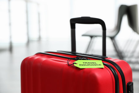 Red suitcase with TRAVEL INSURANCE label indoors, closeupの写真素材