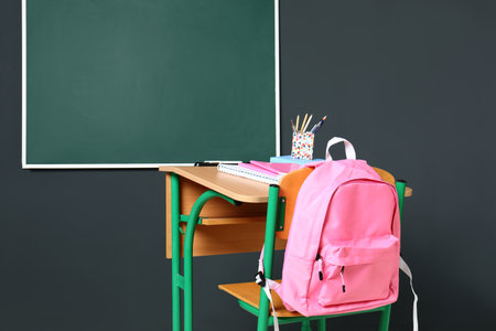 Wooden school desk with stationery and backpack near blackboard on grey wallの写真素材