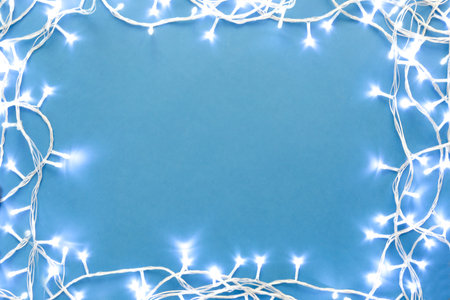 Frame made with Christmas lights on blue background, top view. Space for textの写真素材
