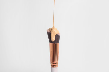 Liquid foundation pouring on makeup brush against white background