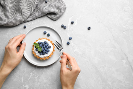 Woman eating blueberry tart at marble table, top view with space for text. Delicious pastriesの写真素材