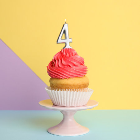 Birthday cupcake with number four candle on stand against color backgroundの写真素材