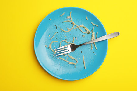 Dirty plate with food leftovers and fork on yellow background, top viewの写真素材