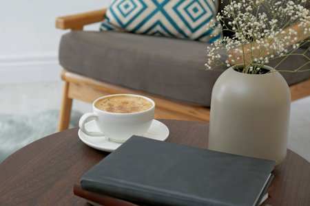 Cup of coffee and vase with flowers on wooden table in modern living room interiorの写真素材
