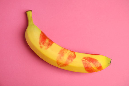 Top view of fresh banana with red lipstick marks on pink background. Oral sex conceptの写真素材