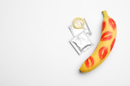 Condoms and banana with lipstick kiss marks on white background, top view. safe sexの写真素材