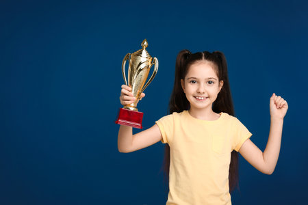 Happy girl with golden winning cup on dark blue background. Space for textの写真素材