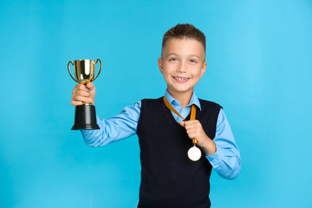 Happy boy in school uniform with golden winning cup and medal on blue backgroundの写真素材
