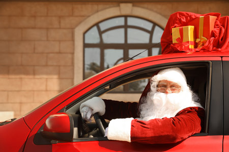 Authentic Santa Claus with bag full of presents on roof driving modern car, outdoorsの写真素材
