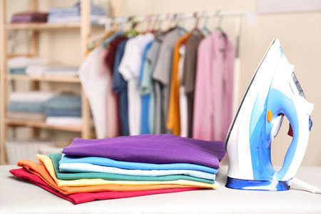 Modern electric iron and folded clothes on board in laundry room. Space for textの写真素材