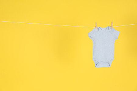 Baby bodysuit hanging on clothes line against yellow background, space for textの写真素材