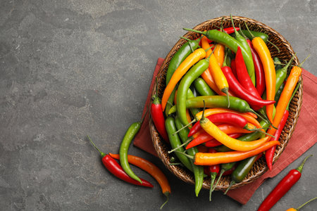 Wicker bowl with different chili peppers on gray table, flat lay. Space for textの写真素材