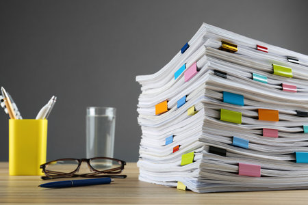 Stack of documents with binder clips and glasses on wooden table against gray backgroundの写真素材