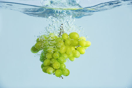 Fresh ripe grapes falling in water on gray backgroundの写真素材