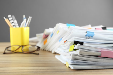 Stack of documents with binder clips and glasses on wooden tableの写真素材