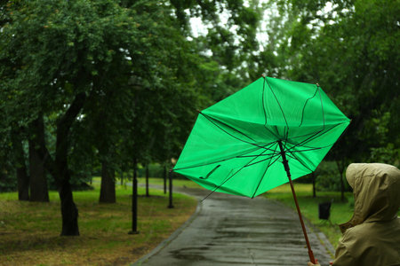 Woman with broken green umbrella in park on rainy dayの写真素材