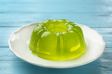 Plate of tasty fruit jelly on blue wooden table, closeup