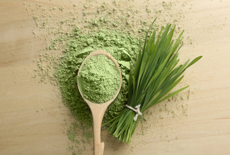 Spoon of wheat grass powder and green sprouts on wooden table, flat layの写真素材