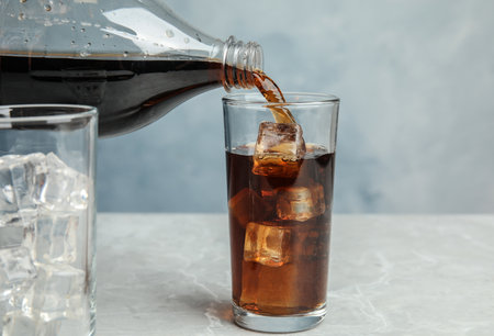 Pouring refreshing soda drink into glass on table against blue backgroundの写真素材