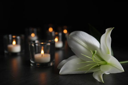 White lily and blurred burning candles on table in darkness, closeup with space for text. funeral symbolの写真素材