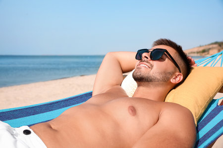 Young man relaxing in hammock on beachの写真素材