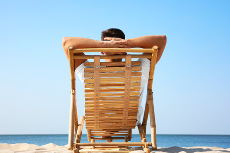Young man relaxing in deck chair on sandy beachの写真素材