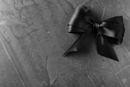 Black ribbon bow on dark gray stone surface, top view with space for text. funeral symbolの写真素材