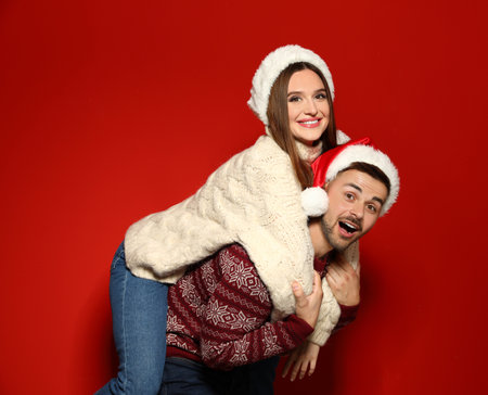 Couple wearing Christmas sweaters and Santa hats on red backgroundの写真素材