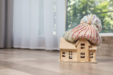 Wooden house model in hat on floor indoors, space for text. heating efficiencyの写真素材