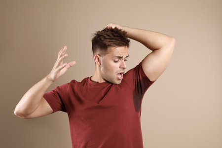 Young man with sweat stain on his clothes against beige background. Using deodorantの写真素材