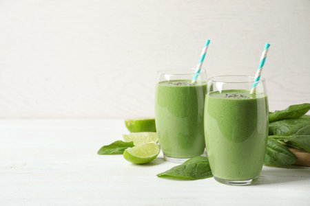 Glasses of healthy green smoothie with fresh spinach on white wooden table against light background. Space for textの写真素材