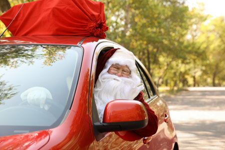Authentic Santa Claus with bag full of presents on roof driving modern car, outdoorsの写真素材