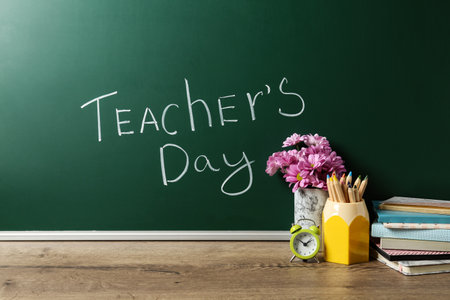 Green chalkboard with inscription TEACHER'S DAY and vase of flowers on wooden tableの写真素材