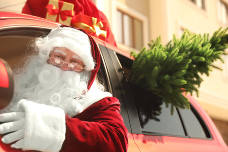 Authentic Santa Claus with fir tree and bag full of presents on roof driving modern car, outdoorsの写真素材