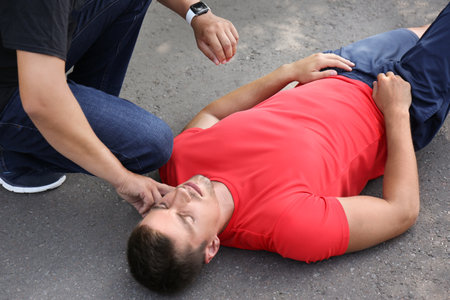 Passerby checking pulse of unconscious young man outdoorsの写真素材